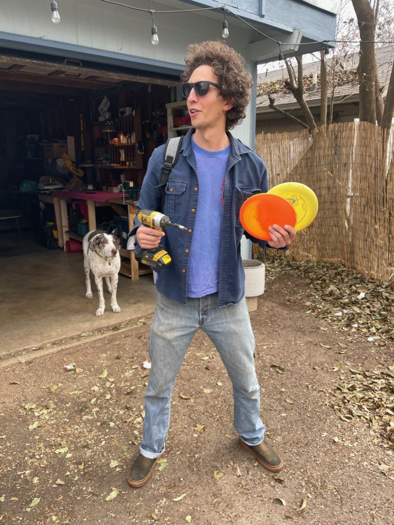 Bass player Jon holding frisbee golf discs and a hand drill