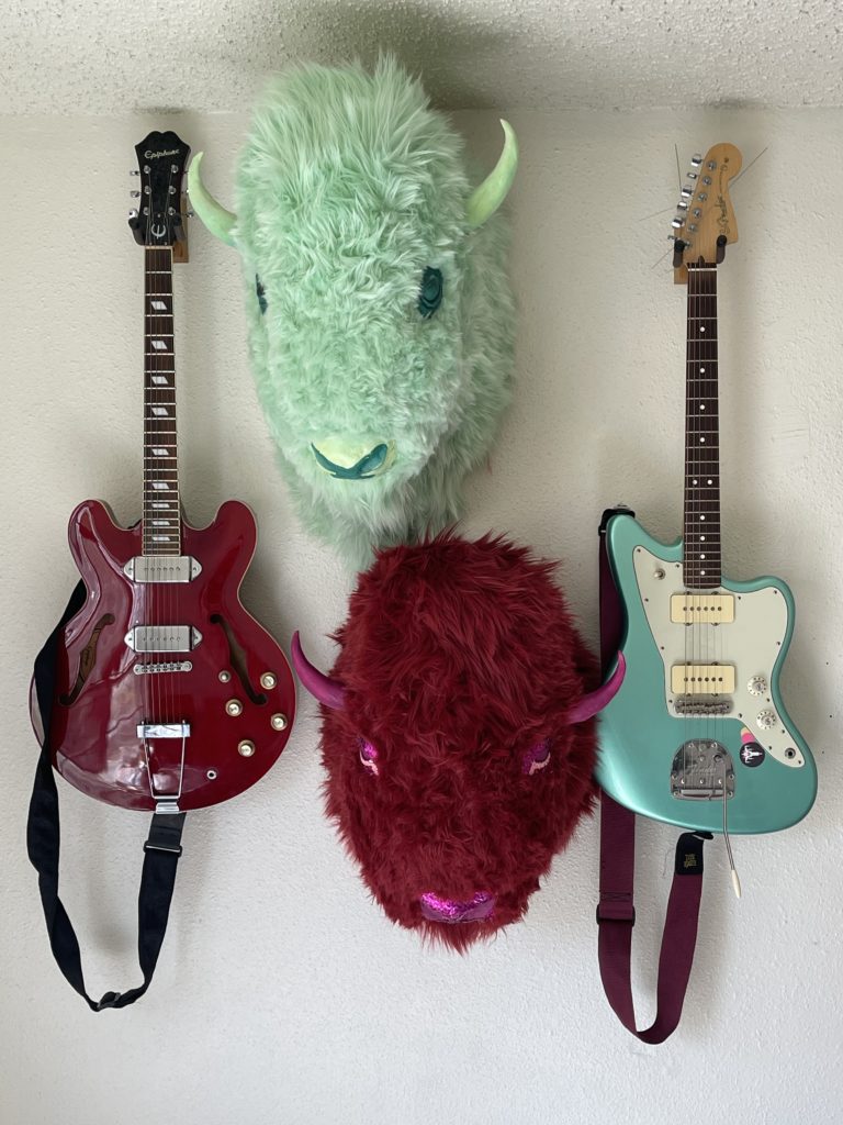 aqua and maroon buffalo heads mounted with guitars on a wall
