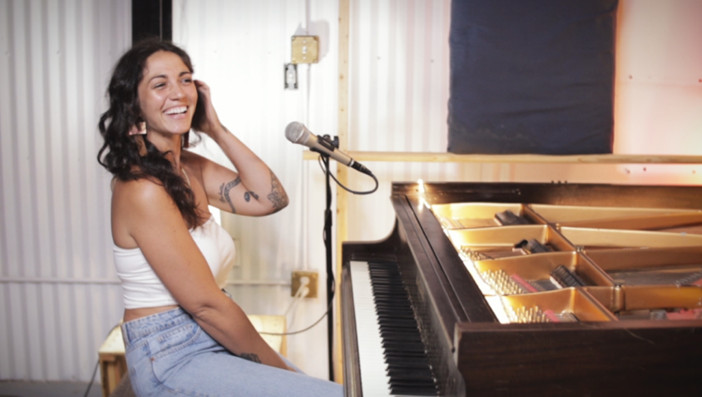 woman with long dark hair smiling at piano with microphone