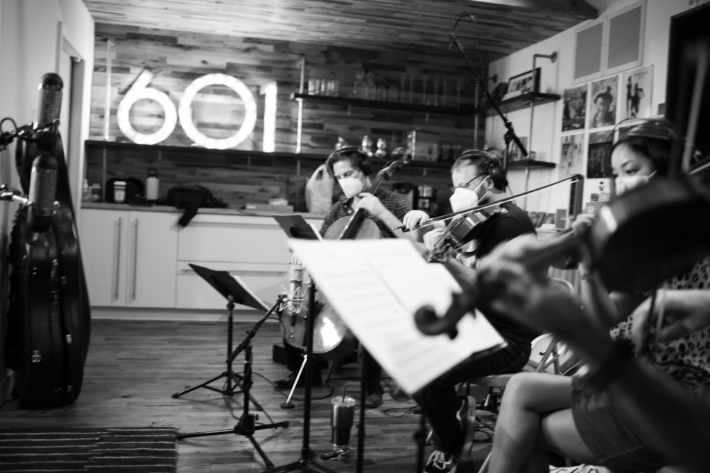black and white image of string players recording in a studio with 601 in bright lights
