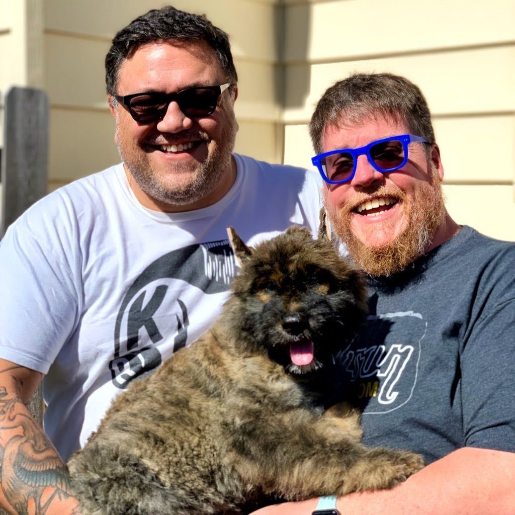 a smiling couple in sunglasses with their dog