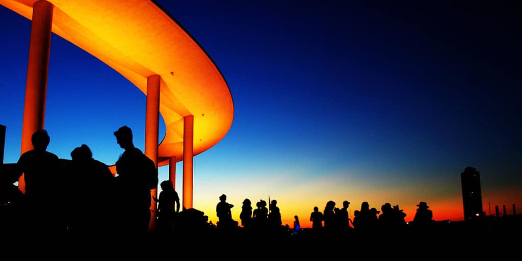 a full crowd at sunset silhouetted against an orange Long Center ring beam and a darkening sky