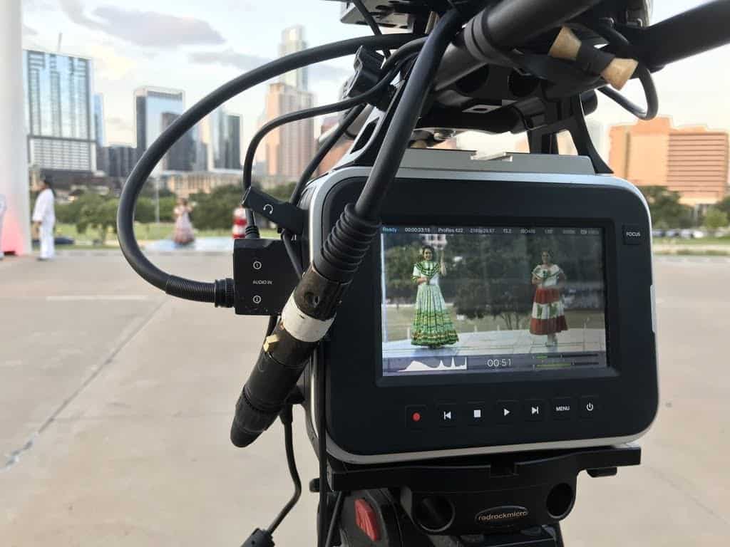 A view through a film camera of two news anchors in traditional Mexican dress