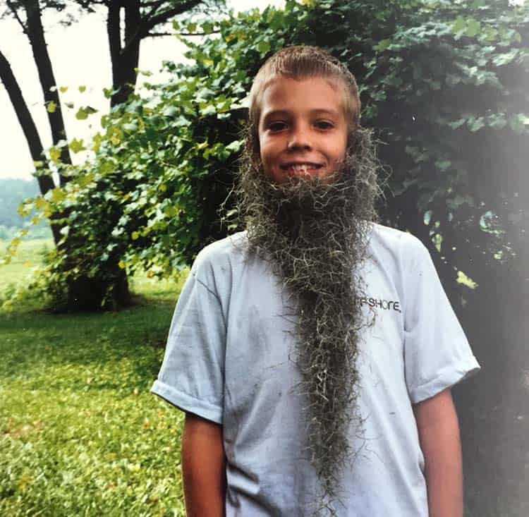 Jordan as a young boy in a greenspace comically large beard made of moss