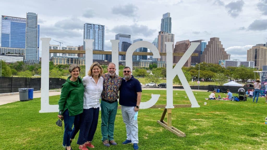 Lynn stands with her partner and friends on the Long Center lawn in front of a big blocky LUCK sign