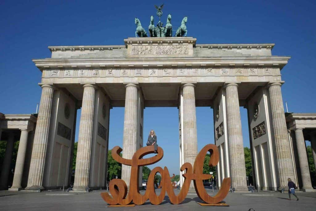 The sculpture, reddish brown "love" in front of Berlin's Brandenburg Gate with Mia sitting atop it