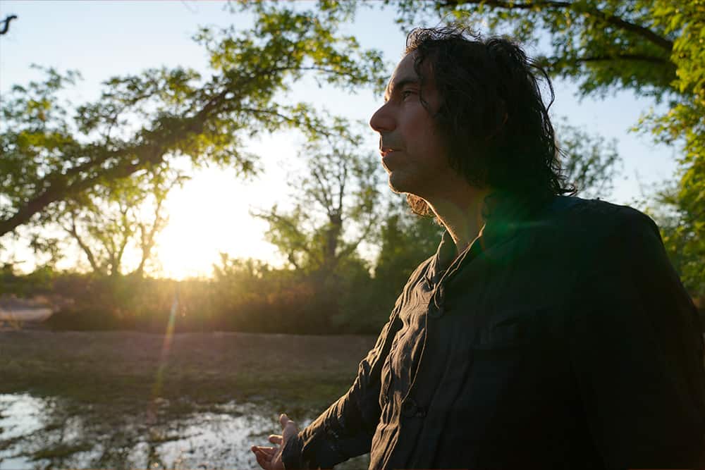 David Garza looks out pensively on a lake at sunset