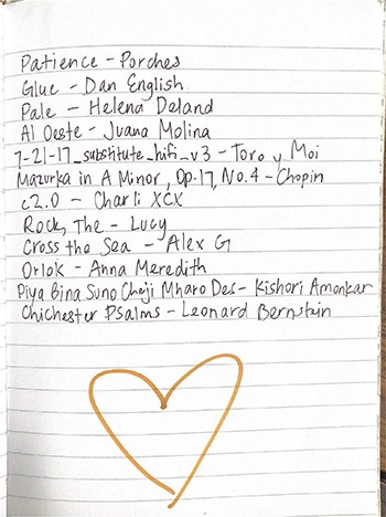 A piece of spiral notepaper with a handwritten list of songs and a gold heart