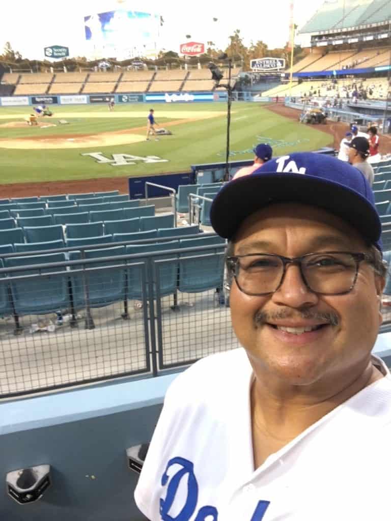 Matt poses in Dodgers gear in front of the field, with a big smile