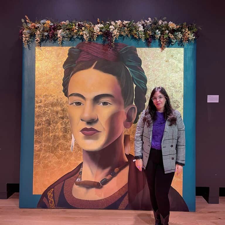 Olivia stands next to a larger than life portait of artist Frida Kahlo
